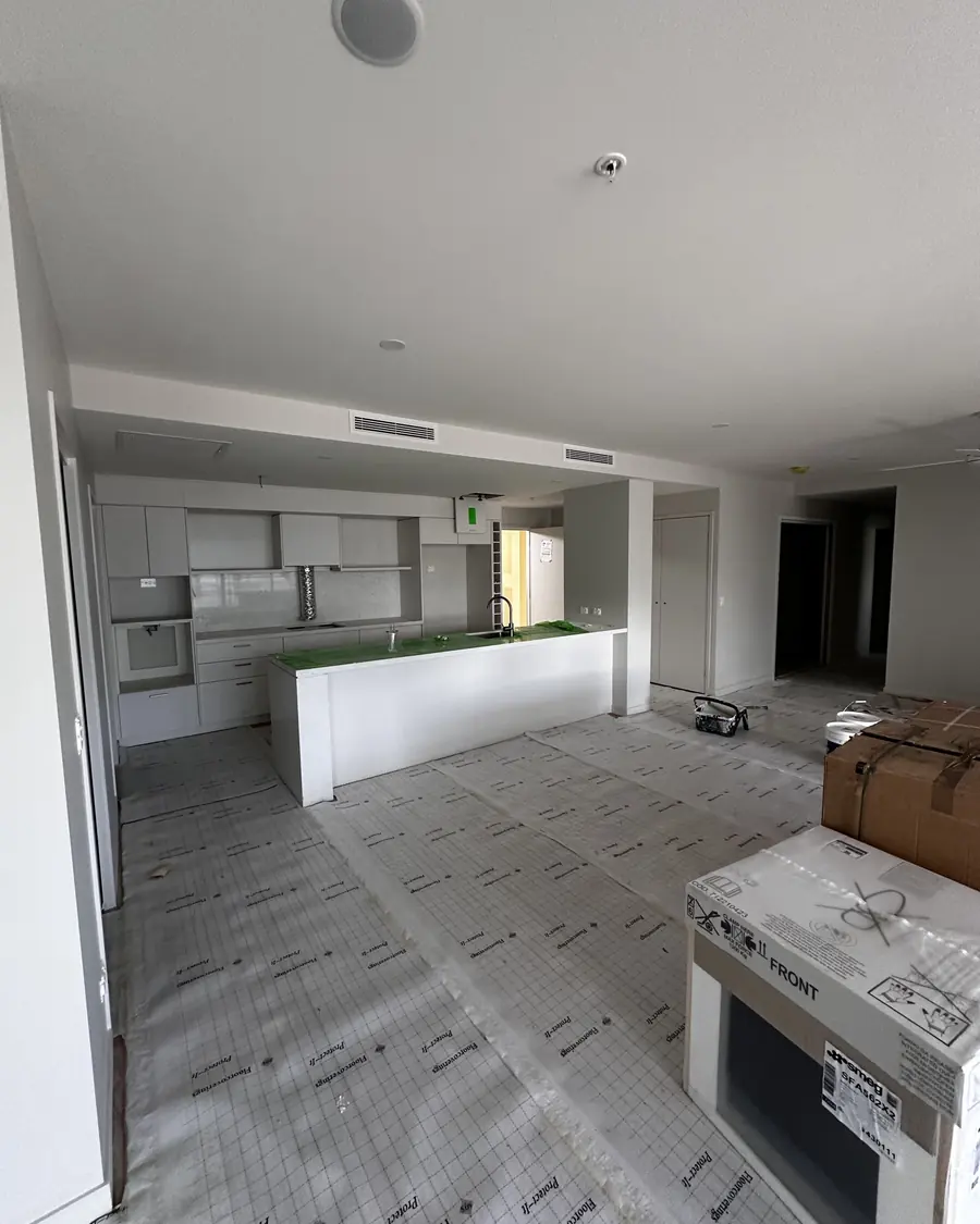 Open-plan apartment with floors and kitchen benchtop masked and protected before painting